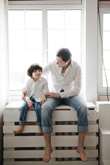 Fototapeta premium Handsome man and his son. Father and little son are sitting in white shirts and jeans. Father's day