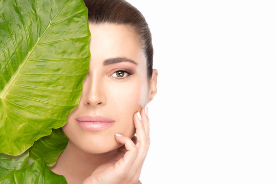 Skin care concept with a young beautiful woman touching her face behind a leaf. Spa beauty portrait