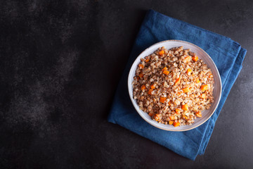 Boiled buckwheat cereal with carrot, parsley and butter in a bowl on a dark background. Traditional Russian dish on dark background with copy space