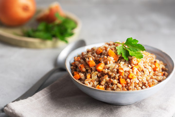 Boiled buckwheat cereal with carrot, parsley and butter in a bowl on a dark background. Traditional Russian dish on gray background