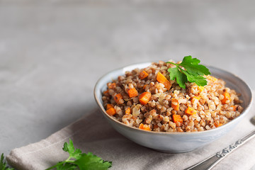 Boiled buckwheat cereal with carrot, parsley and butter in a bowl on a dark background. Traditional Russian dish on gray background with copy space