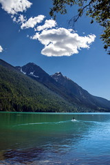 Mountain Lake in Provincial Park, Green water and forested slope in the background  blue sky with white clouds,  man driving scooter