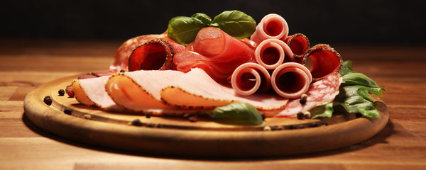 Food tray with delicious salami, pieces of sliced ham, sausages,salad and vegetable. Meat platter with selection