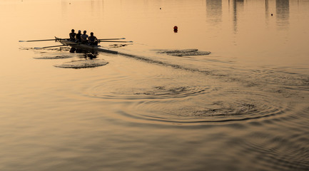 Sunrise lights up team of four rowers in canoe practicing in London Docklands © steheap