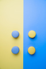 Sweet tasty blue and yellow french macaron cakes on yellow and blue background.