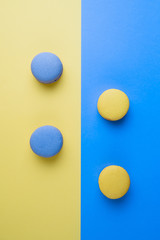 Sweet tasty blue and yellow french macaron cakes on yellow and blue background.