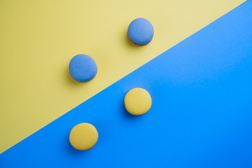 Sweet tasty blue and yellow french macaron cakes on yellow and blue background.