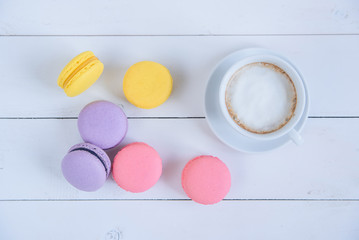 Sweet delicious colorful macarons and cup of coffee on white wooden background.