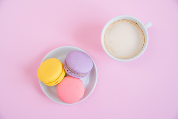 Tasty sweet macarons on the plate and cup of fragrant morning coffee. French macaroons on pink background.