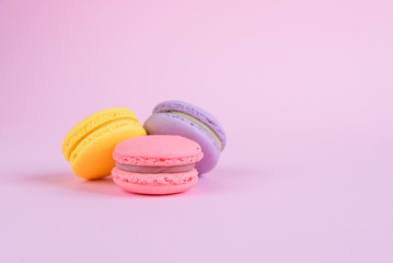Tasty violet, pink and yellow french macaron cakes on pink background.
