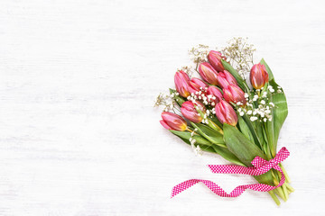Pink tulips and gypsophila bouquet decorated with ribbon on white background. Copy space, top view