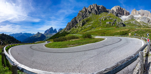 Tourists in cars drive away from the sharp hairpin turn in the sunny mountains.