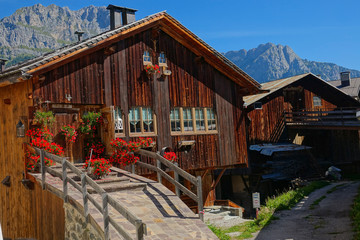 Empty concrete trail runs past two traditional wooden houses in the Dolomites.