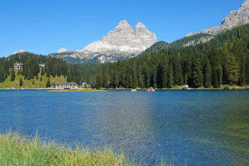 Tourists in boats wandering around the tranquil lake in the sunny Dolomites.