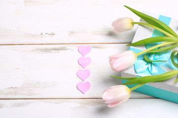 Fototapeta na wymiar pink tulips on a gift box on a white wooden table