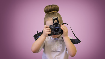 A girl in business dress holds a reflex camera in front of her face. The child wants to take a picture. The kid holds her finger on the shutter button.