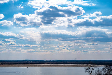 Fototapeta na wymiar View of the Amur river against the blue sky with white beautiful clouds. Bright spring sun. Russia, Khabarovsk.