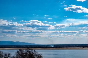 View of the Amur river against the blue sky with white beautiful clouds. Bright spring sun. Russia, Khabarovsk.