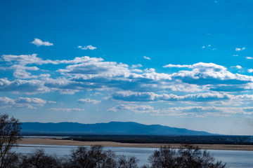 View of the Amur river against the blue sky with white beautiful clouds. Bright spring sun. Russia, Khabarovsk.