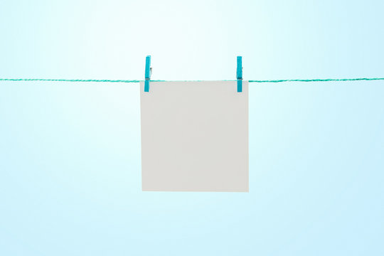 Empty white note paper hanging on rope against sunny blue sky with copy space