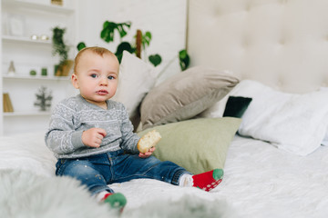 Cute little toddler boy sitting on bed holding a snack