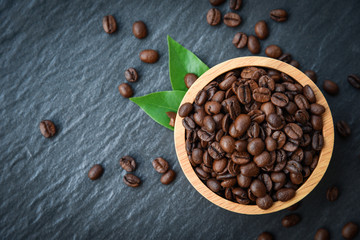 Roasted coffee beans on wooden bowl with green leaf and dark background - top view