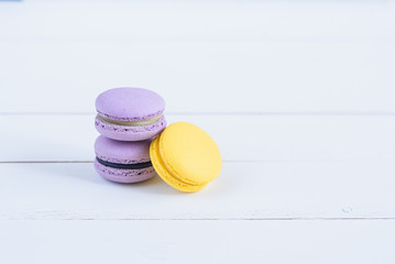 Delicious violet and yellow macarons on white wooden background.