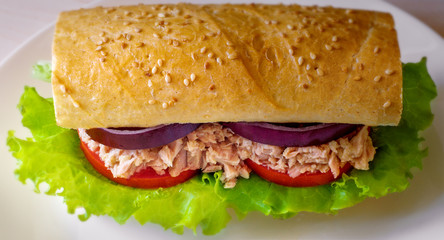 Tuna sandwich on wooden table. Blurred background. White plate. Tuna, lettuce, onion, tomato, bread. Closeup.