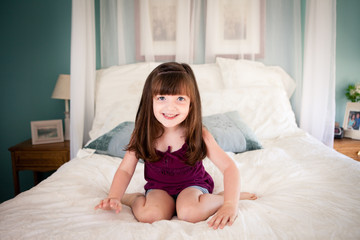 Little Girl Sitting on Bed in Bedroom at Home