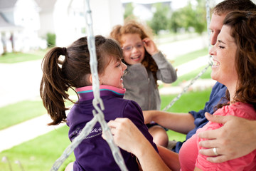 Happy Family Sitting on Bench Swing Together Outside Their Home