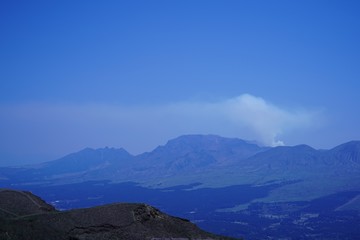 Fototapeta na wymiar 噴煙を放つ阿蘇山と阿蘇町の風景