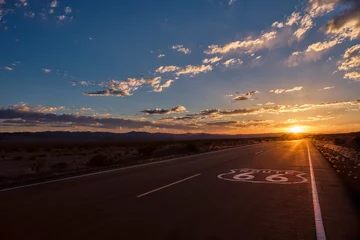 Gardinen Das Straßenschild der Route 66 im Vordergrund und die abnehmende Perspektive der Straße, die zu einem dramatischen Sonnenuntergang in der Mojave-Wüste außerhalb von Amboy, Kalifornien, führt. © Ben