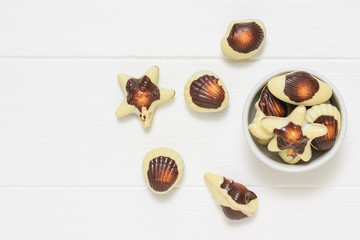 White bowl with sweets in the form of sea shells on a white rustic table. Flat lay.