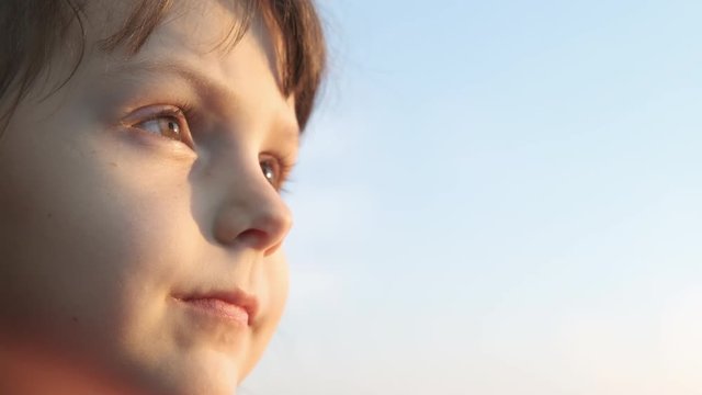 Portrait of a child against the sky. Adorable little girl looks at the sunset in the window.