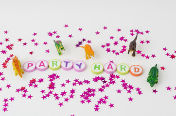 Party hard made from colorful letters, toy little dinosaurs and stars confetti on white background
