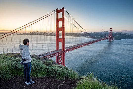 Asian man photographer and tourist enjoy looking at Golden Gate Bridge during sunrise, Iconic bridge and famous landmark of San Francisco, California, USA. Travel photography concept