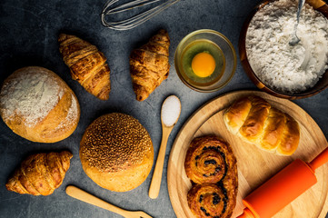 Freshly baked bread on wooden table,Bakery Concept- gold rustic crusty loaves of bread and buns on black chalkboard background. captured from above (top view, flat lay. Layout with copy space