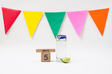 Wooden cube calendar with cinco de mayo date, tequila shot glass, lemon and colorful flags on white background
