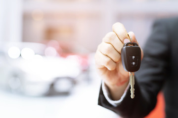 Business man hand holding car key front with car in showroom on background. transport dealership...
