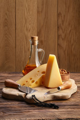 Two types of cheeses - parmesan and gouda with walnuts and honey on wooden board with cheese knives