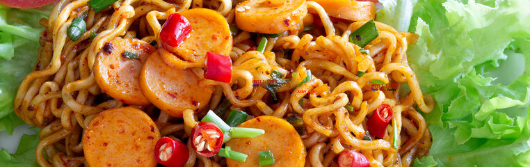 Stir fried spicy yellow noodle with sausage in white dish on gray wooden table.