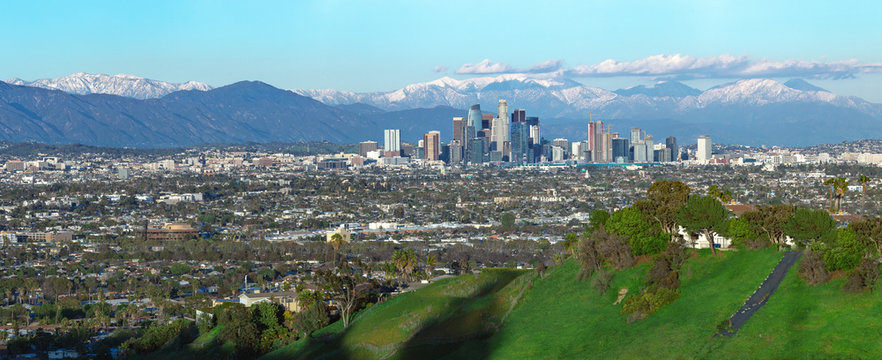 Panoramic view of the city of Los Angeles California with snowy mountain caps showing the end of the drought due to climate change.  The wide view shows Hollywood and Downtown.