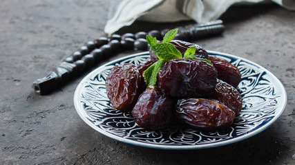Ramadan kareem food concept. Fresh Dates, rosary beads and tea on dark concrete background. Banner image