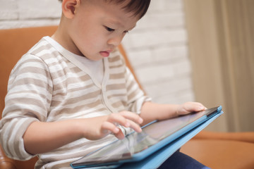 Confused aggressive Asian 2 - 3 years old toddler boy child using tablet pc playing game while waiting for his flight at Airport lounge, Gadget addicted children,Traveling with kid concept