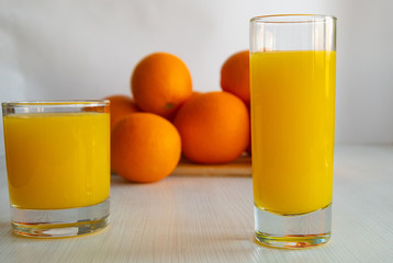 A glass of orange juice is on the table next to oranges.
