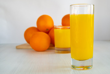 A glass of orange juice is on the table next to oranges.