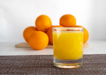A glass of orange juice is on the table next to oranges.