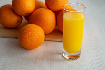 A glass of orange juice is on the table next to oranges.
