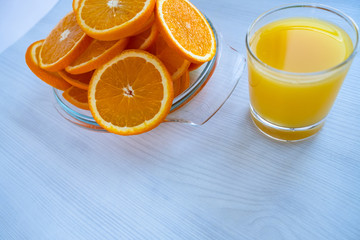 A glass of orange juice is on the table next to oranges.