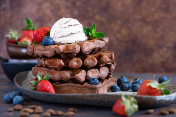 Chocolate and vanilla Belgian waffles with fresh berries on a ceramic plate on brown background. Sweet breakfast